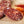 Load image into Gallery viewer, A close up of salami slices displaying the fat marbling, herbs and spices. The salami slices are on a wood cutting board with blurred herbs and spices in the background.