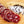 Load image into Gallery viewer, A close up of salami slices displaying the fat marbling, herbs and spices. The salami slices are on a wood cutting board with herbs and spices blurred in the background.