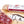Load image into Gallery viewer, A close up of saucisson sec salami in packaging and on a cutting board with blurred salami slices, herbs and spices in the foreground.