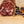 Load image into Gallery viewer, A photo looking directly at a slice of salami taken close up so you can see the fat, herbs and spices. The salami slices are on a wood cutting board with juniper berries and other spices to the right of them.