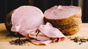 il porcellino salumi's maple mustard glazed berkeley ham on a cutting board with slices in the foreground.