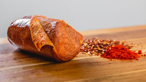 A close up side shot of 'nduja salami on a cutting board with spices next to it.