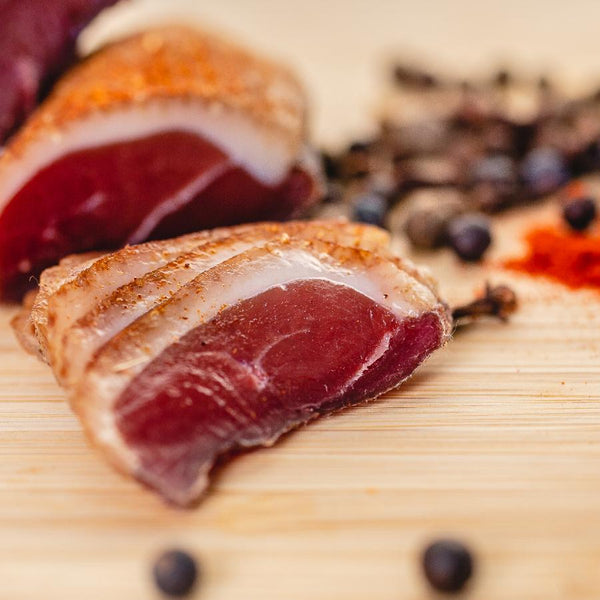 A close up picture of il porcellino salumi's duck prosciutto. The duck prosciutto is cut into slices on a cutting board with whole chubs and spices in the background.