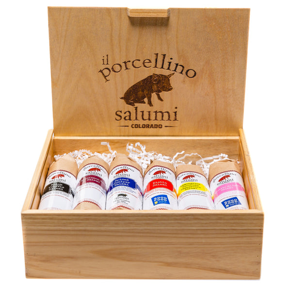 A wooden gift box with il porcellino salumi's logo on the lid and six of their salami displayed in the box.