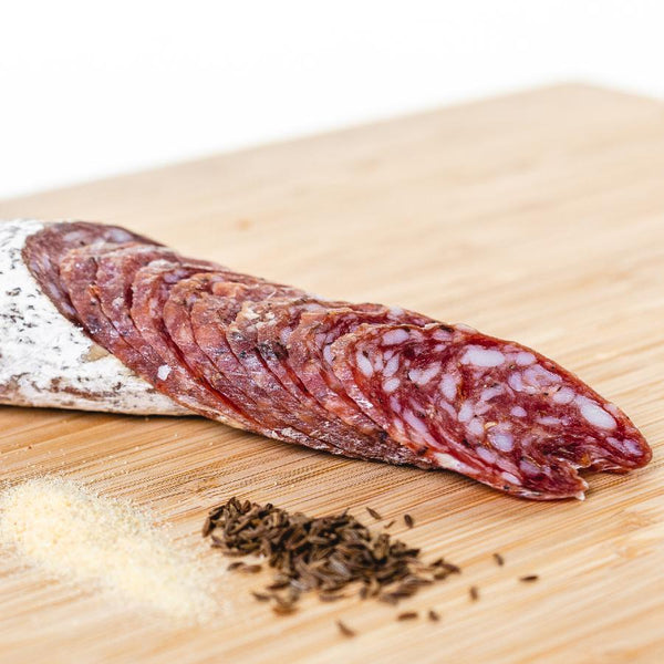Cacciatore salami shot from the side and cut into slices on a cutting board next to herbs and spices.