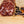 Load image into Gallery viewer, A photo looking directly at a slice of salami taken close up so you can see the fat, herbs and spices. The salami slices are on a wood cutting board with juniper berries and other spices to the right of them. 
